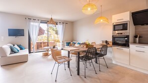A modern kitchen with white cabinets, a dining area with wicker chairs, and a flat-screen TV mounted on the wall. - Apartment 2: Cap Lardier (Roquebrune-sur-Argens)