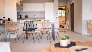 A modern kitchen with white cabinets, a central island, and a dining area with wicker chairs. - Apartment 2: Cap Lardier (Roquebrune-sur-Argens)