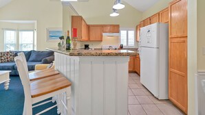 A kitchen with wooden cabinets, a white refrigerator, and a dining area with a table and chairs. - Key West Vibe & Disney Thrills: Tropical Condo w/ Water Park (KIssimmee)