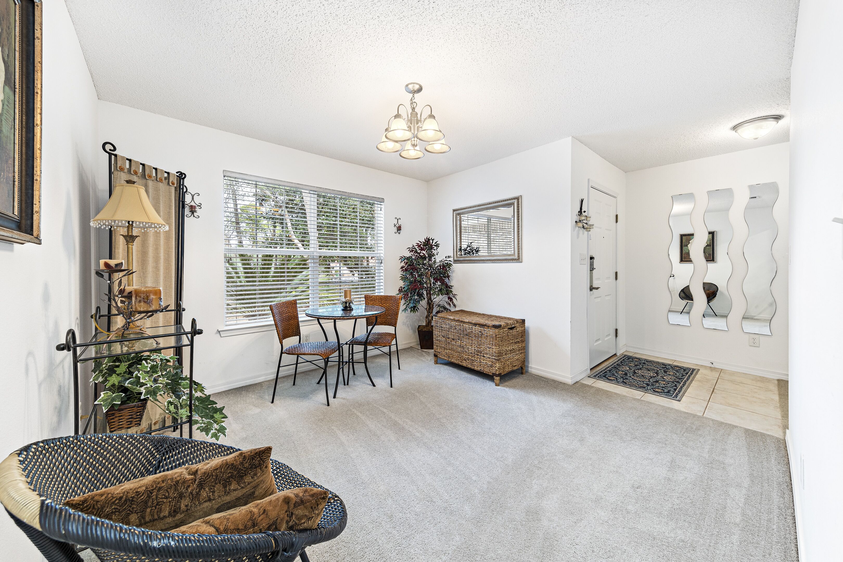A room with a dining table, chairs, a wicker side table, a lamp, a potted plant, and a decorative mirror.