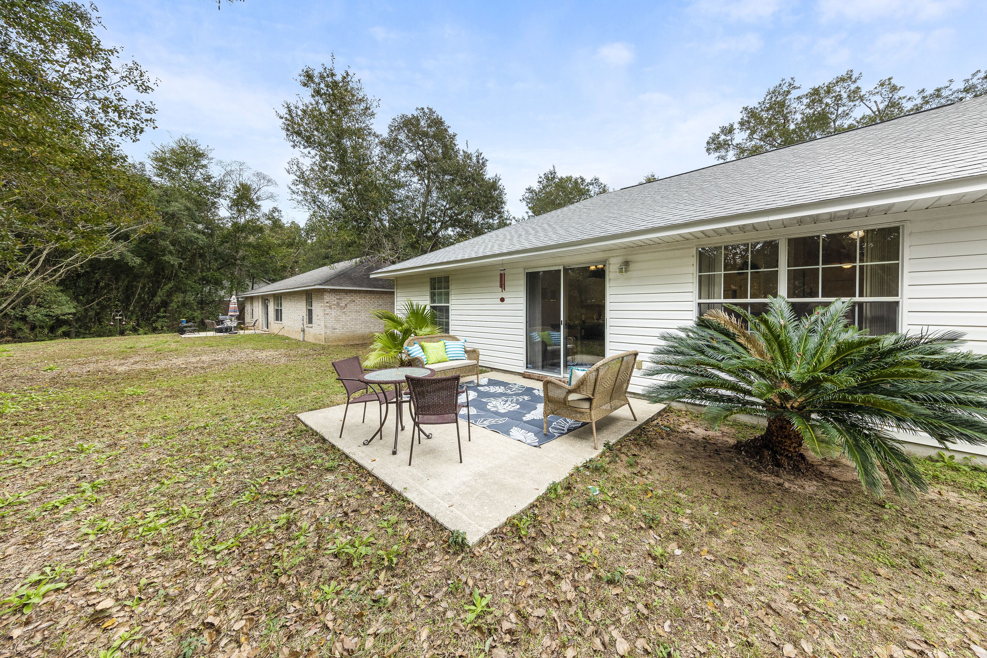 A house with a patio area featuring a table and chairs, a small palm tree, and a covered outdoor seating area.
