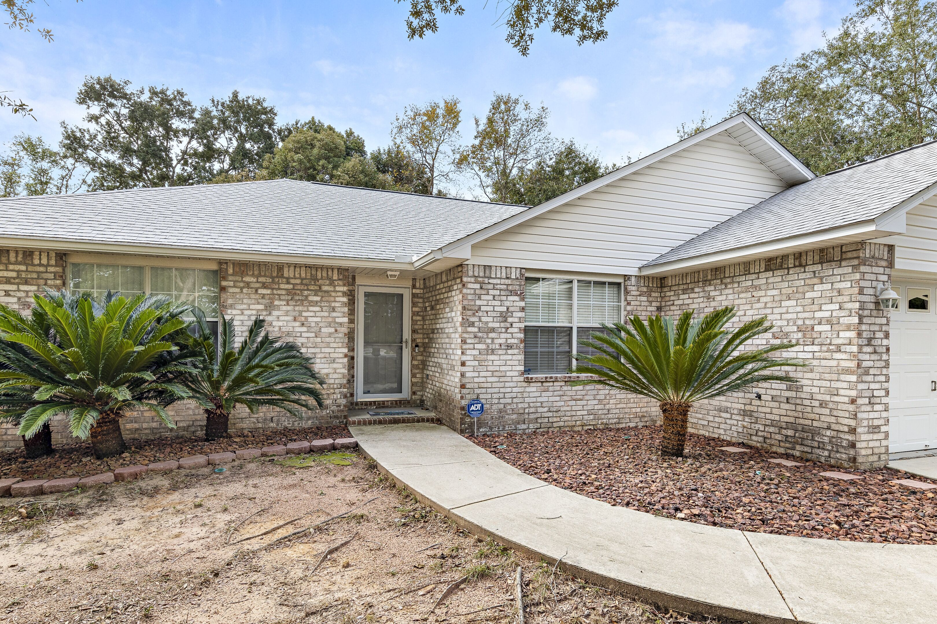 A two-story house with a brick exterior, a front porch, and two palm trees in the front yard.