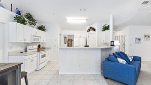 Una cocina moderna con armarios blancos, una isla central y un sofá azul en la sala de estar.