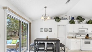 Una cocina moderna con comedor, armarios blancos, horno empotrado y un amplio ventanal con vistas a un jardín.