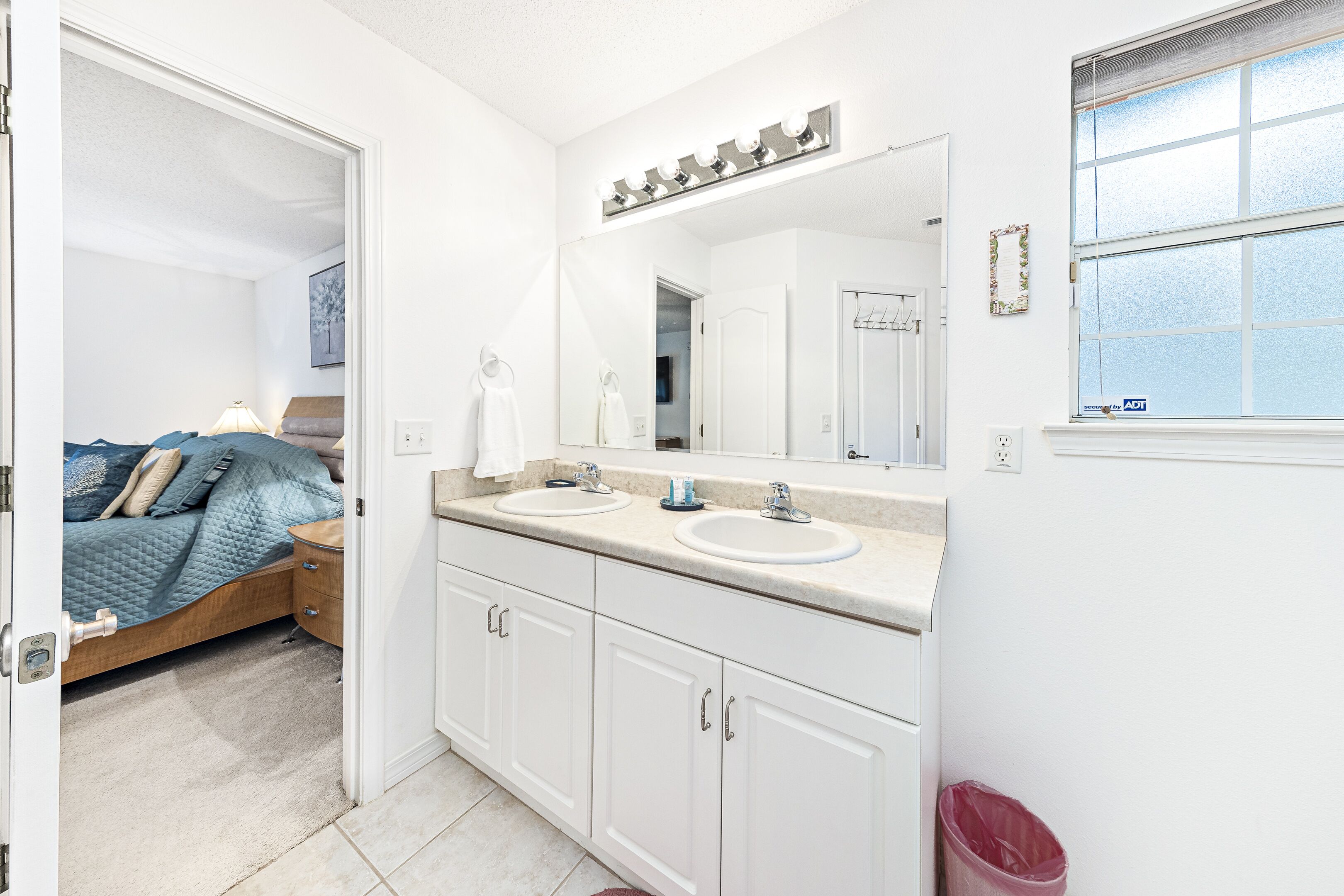 A bedroom with a bed, bedside table, and a large mirror above the sink.
