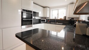 Una cocina moderna con armarios blancos, encimera de granito negro, electrodomésticos de acero inoxidable y un ventanal que proporciona luz natural.