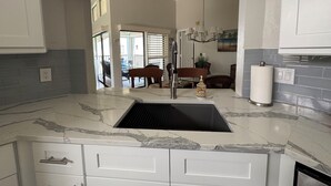 A kitchen with a marble countertop, a sink, and a dining area visible through an open door. - Modern Condo with easy beach access in the heart of Naples Park (Naples)