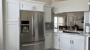 A modern kitchen with white cabinetry, a stainless steel refrigerator, a ceiling fan, and a black rug. - Modern Condo with easy beach access in the heart of Naples Park (Naples)