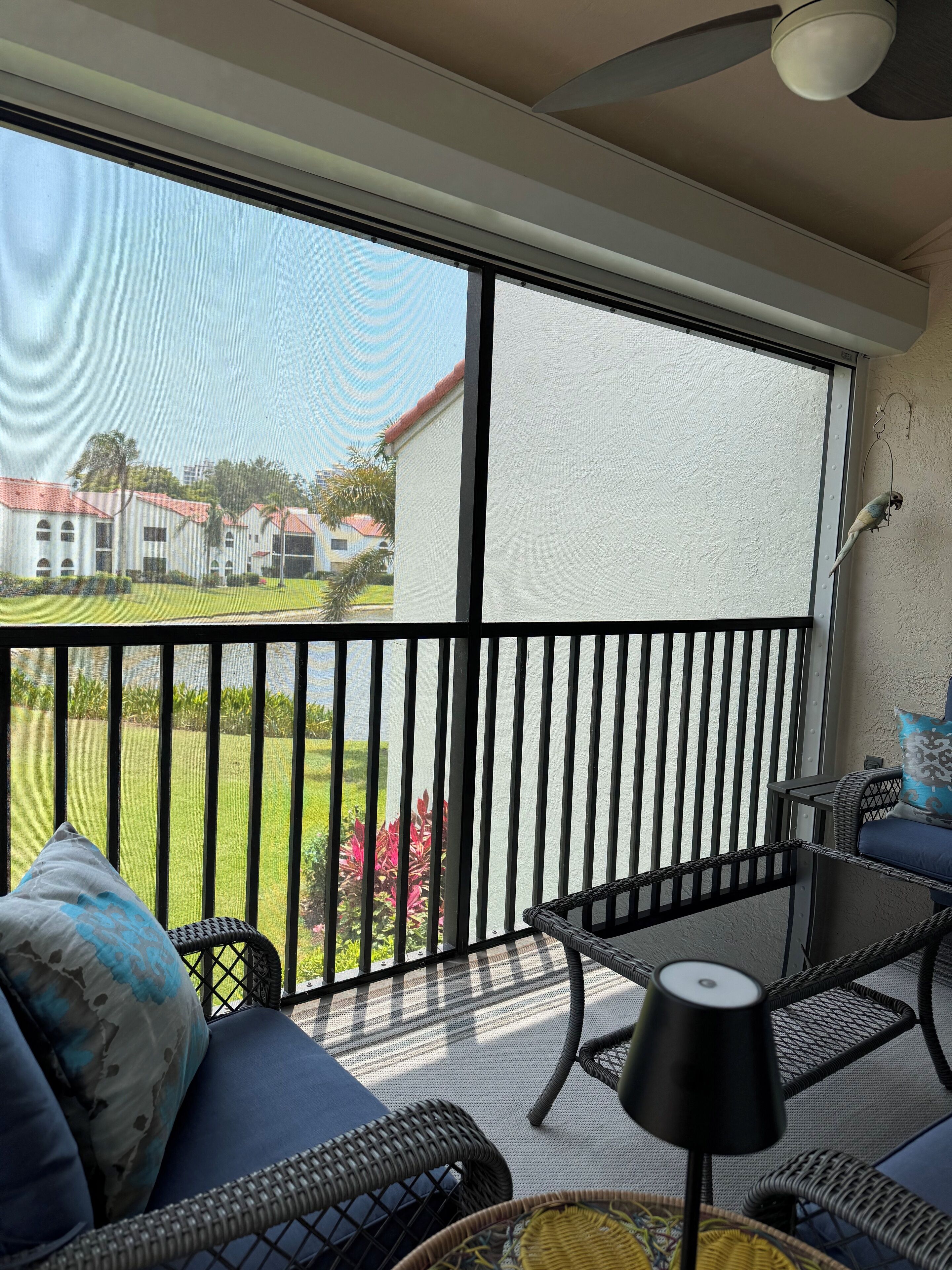 Un balcon doté de meubles en osier, d’un ventilateur de plafond et offrant une vue sur un immeuble et de la verdure.