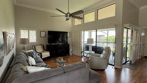 A spacious living room with a grey sofa, a black entertainment unit, and a ceiling fan. - Modern Condo with easy beach access in the heart of Naples Park (Naples)