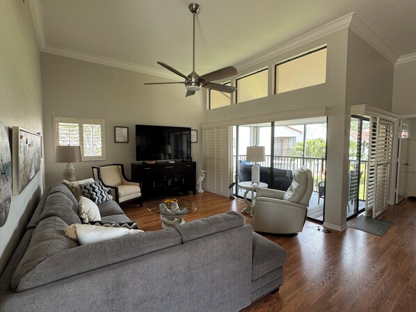 A spacious living room with a grey sofa, a black entertainment unit, and a ceiling fan.