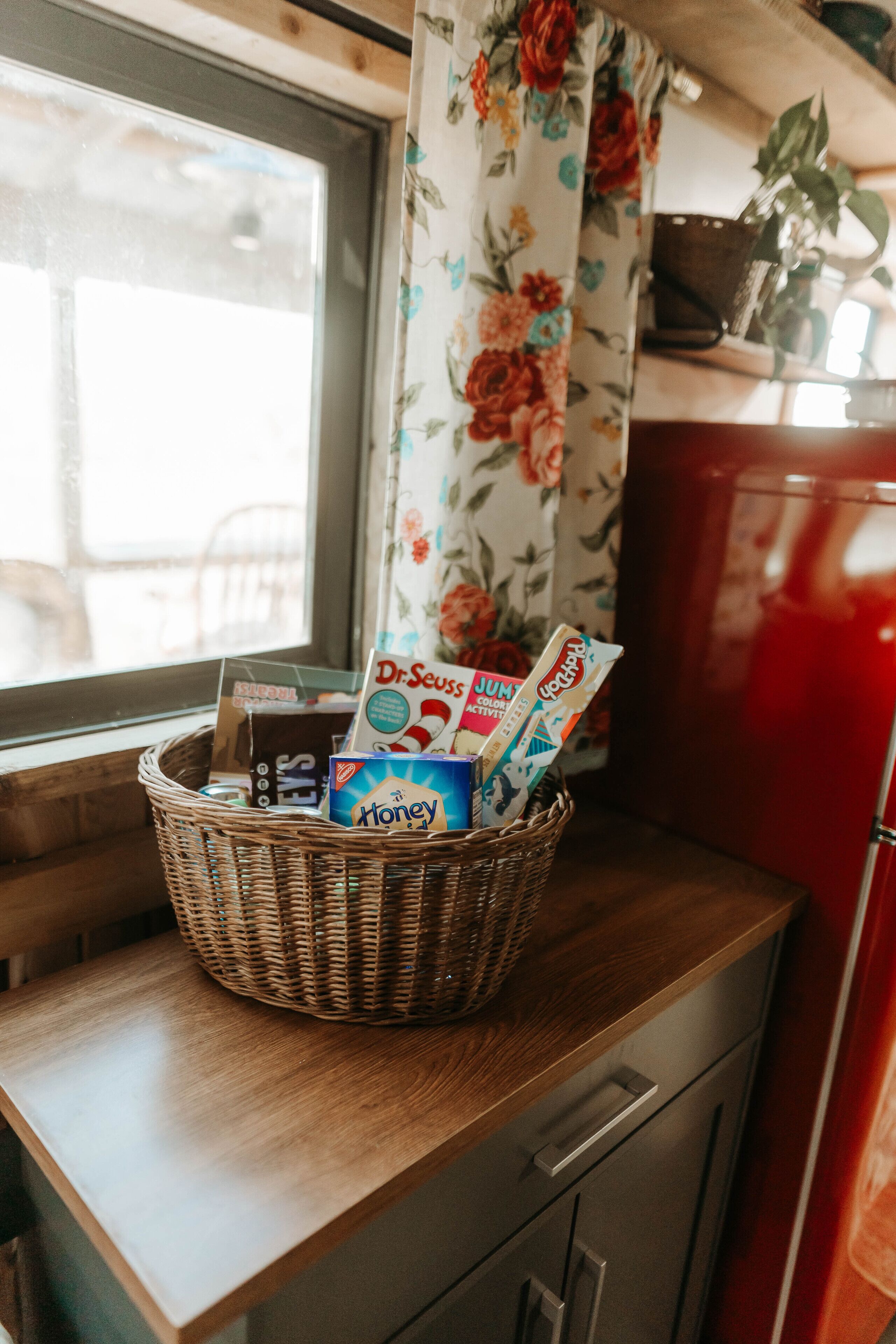 A wicker basket on a wooden counter with various items including a Honey box, Dr. Seuss books, and a JUMPS magazine.