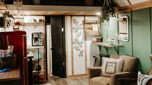 Una habitación acogedora con techo de madera, un refrigerador rojo, un sillón color beige y una mesita con una lámpara.