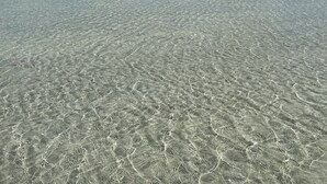 En tydlig vy över en strand med grunt vatten och avlägsna landformationer.