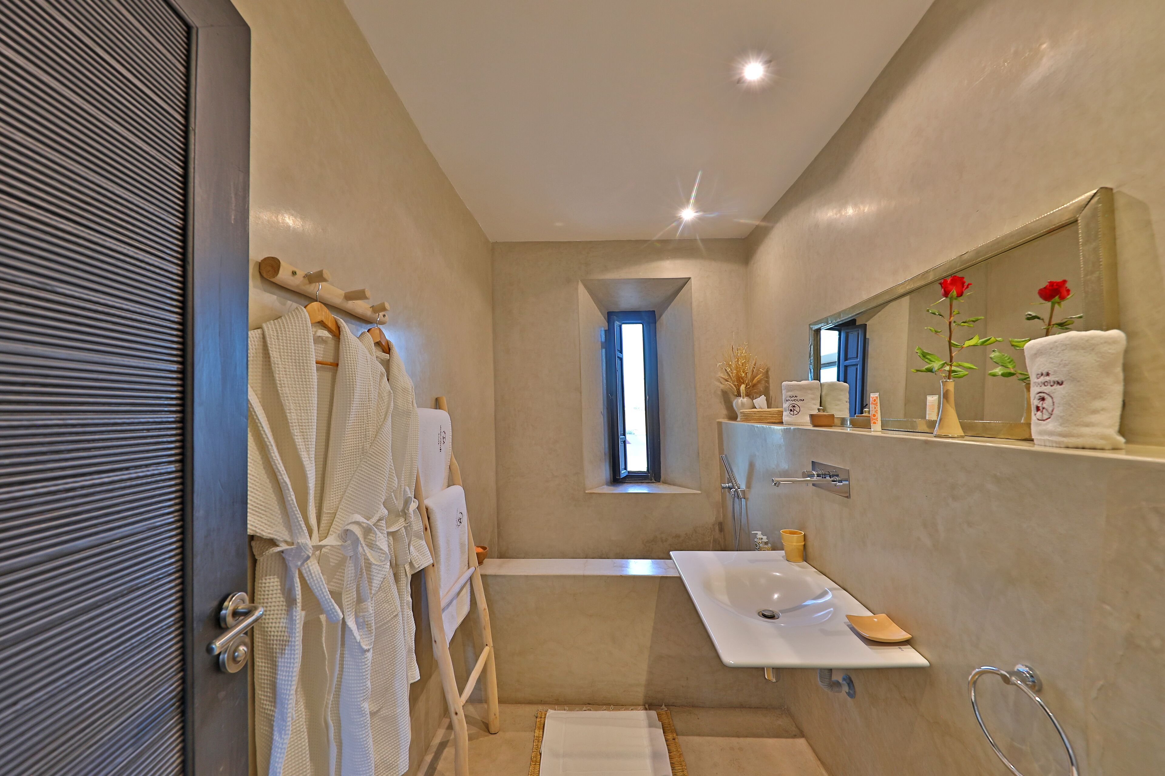 Un baño moderno con bañera, lavamanos y espejo. Hay toallas y un perchero para bata.