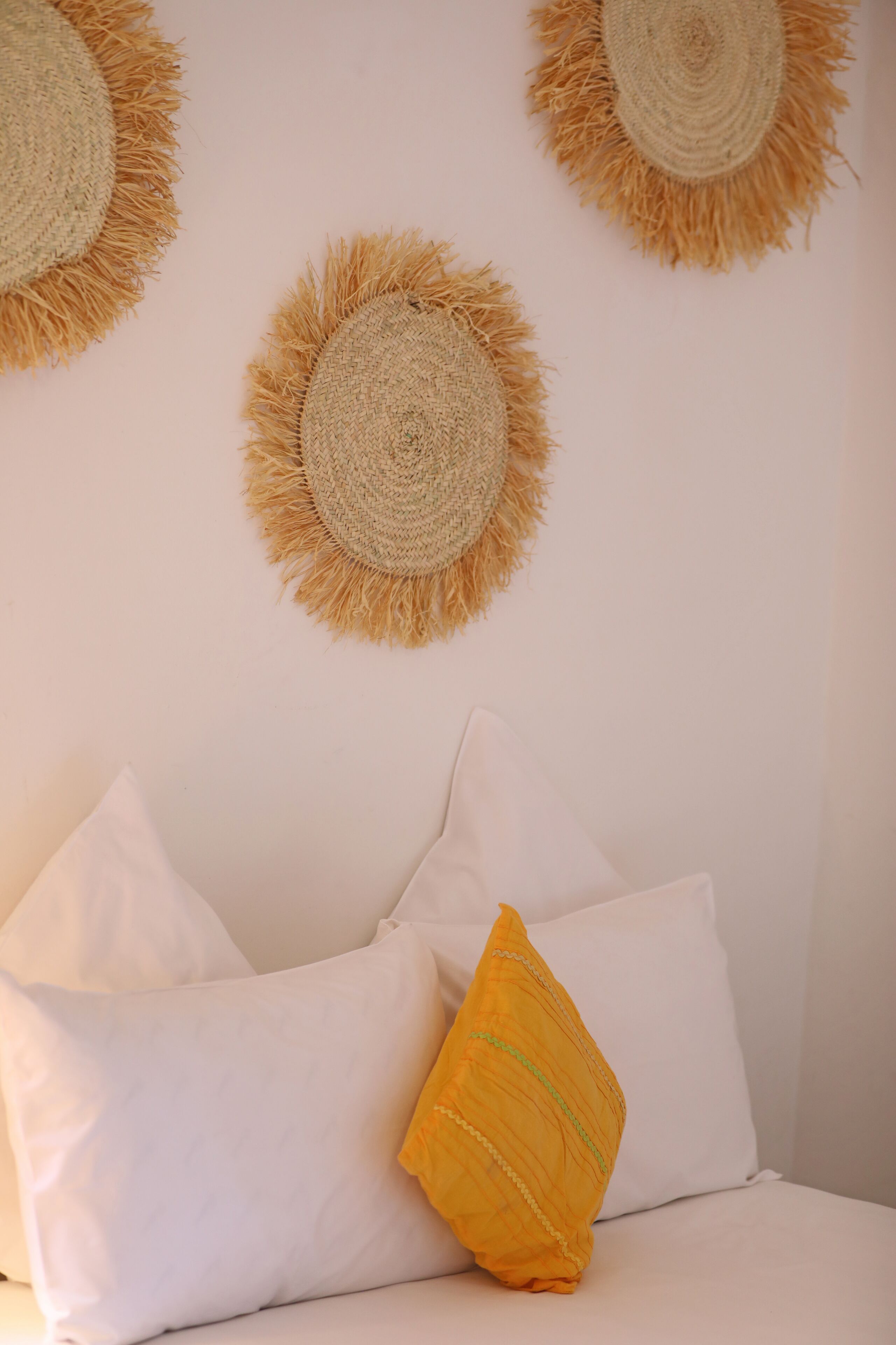 Ein Zimmer mit einem Bett, weißen und gelben Kissen sowie drei gewebten Wanddekorationen.