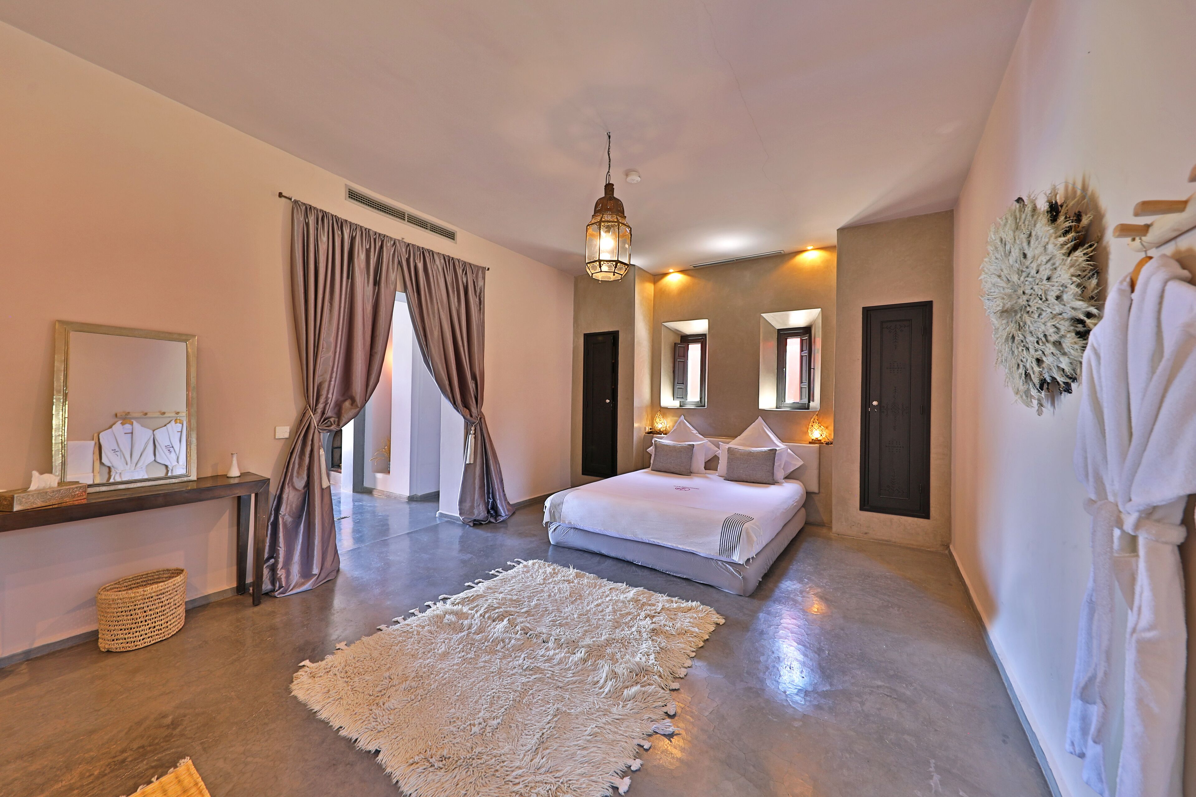 Um quarto espaçoso com uma cama grande, uma mesinha de cabeceira, um espelho e um roupão.