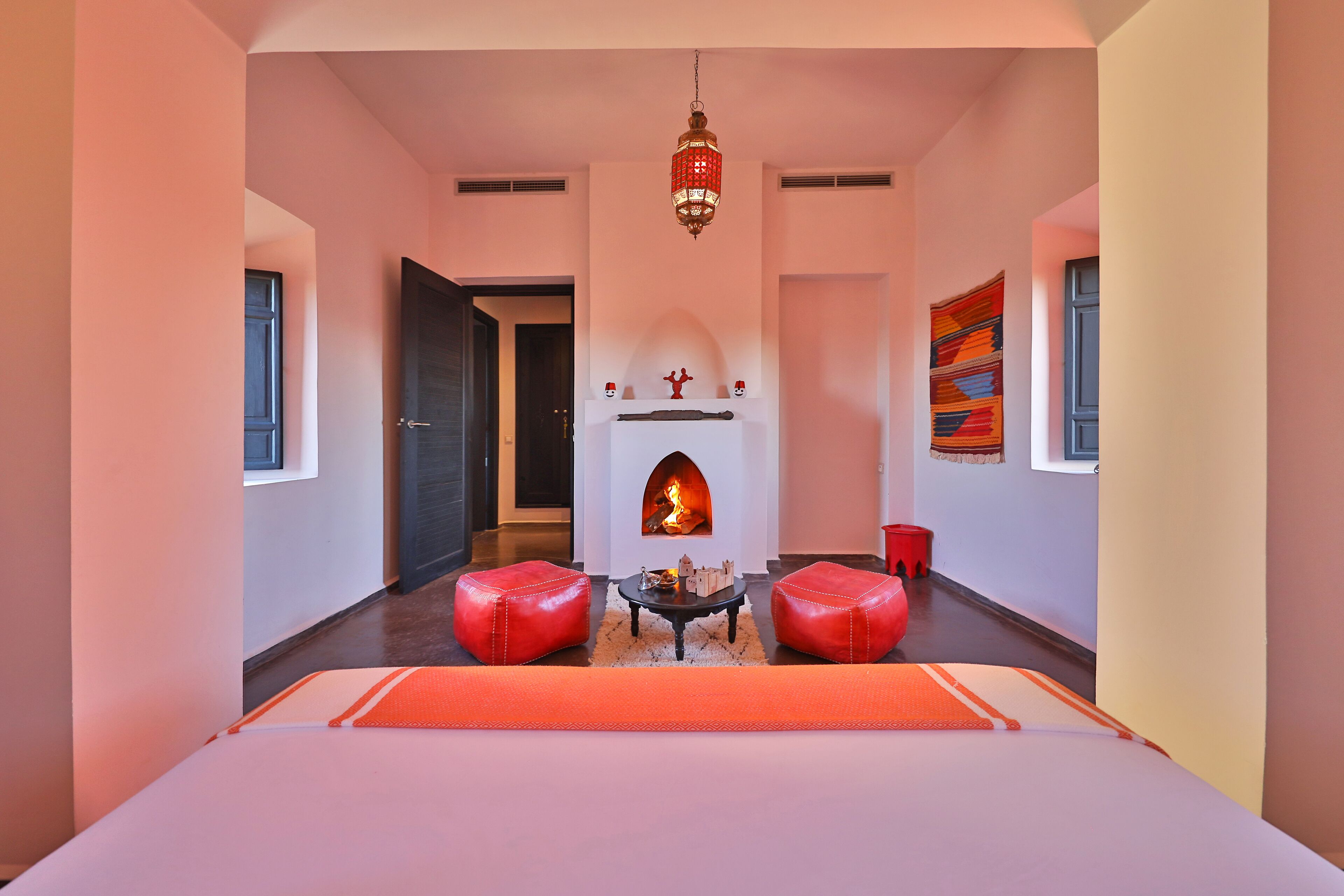 A modern hotel room with a fireplace, red leather ottomans, and a large bed.
