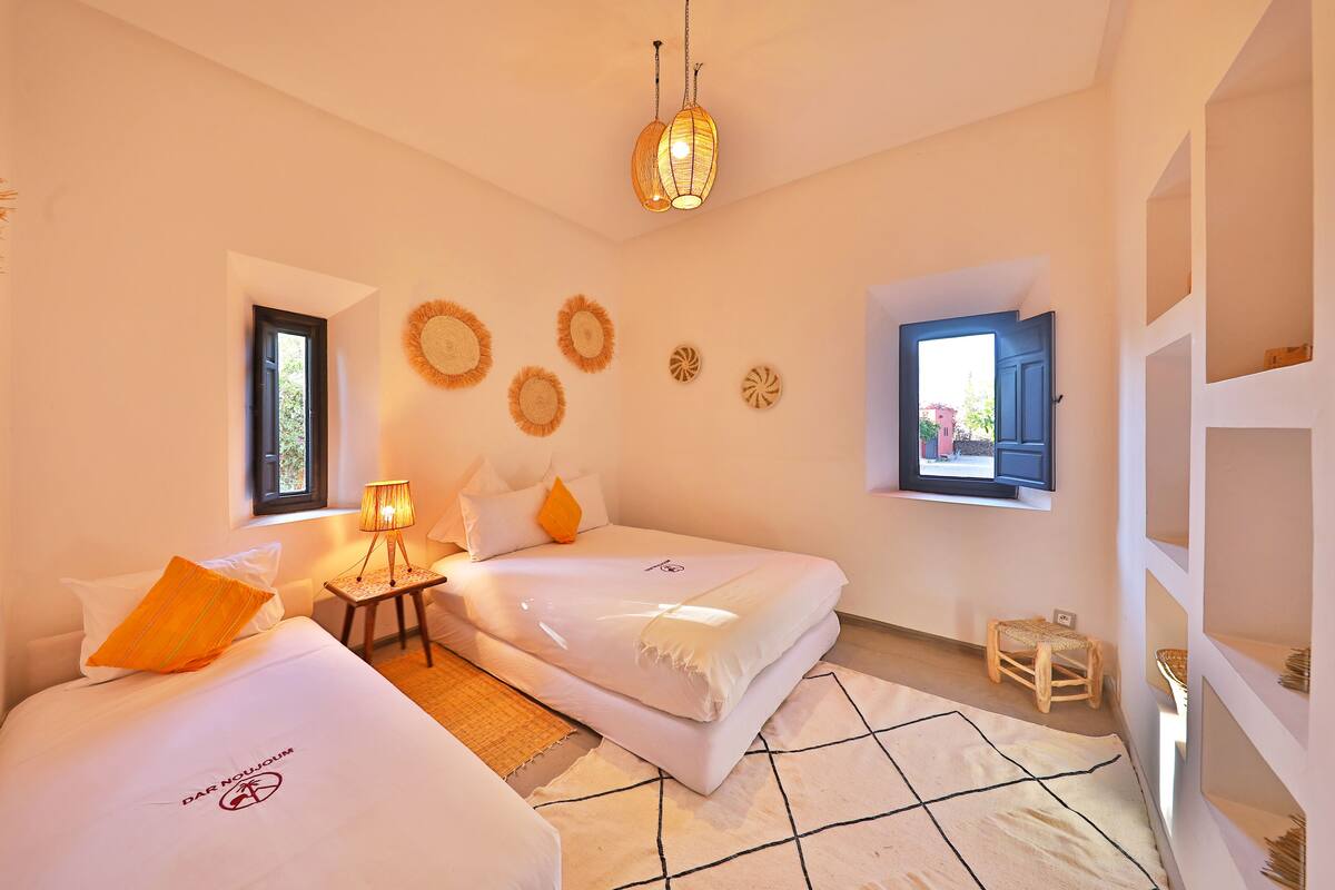 A hotel room with two beds, a small table with a lamp, a window with a view, and decorative wall art.
