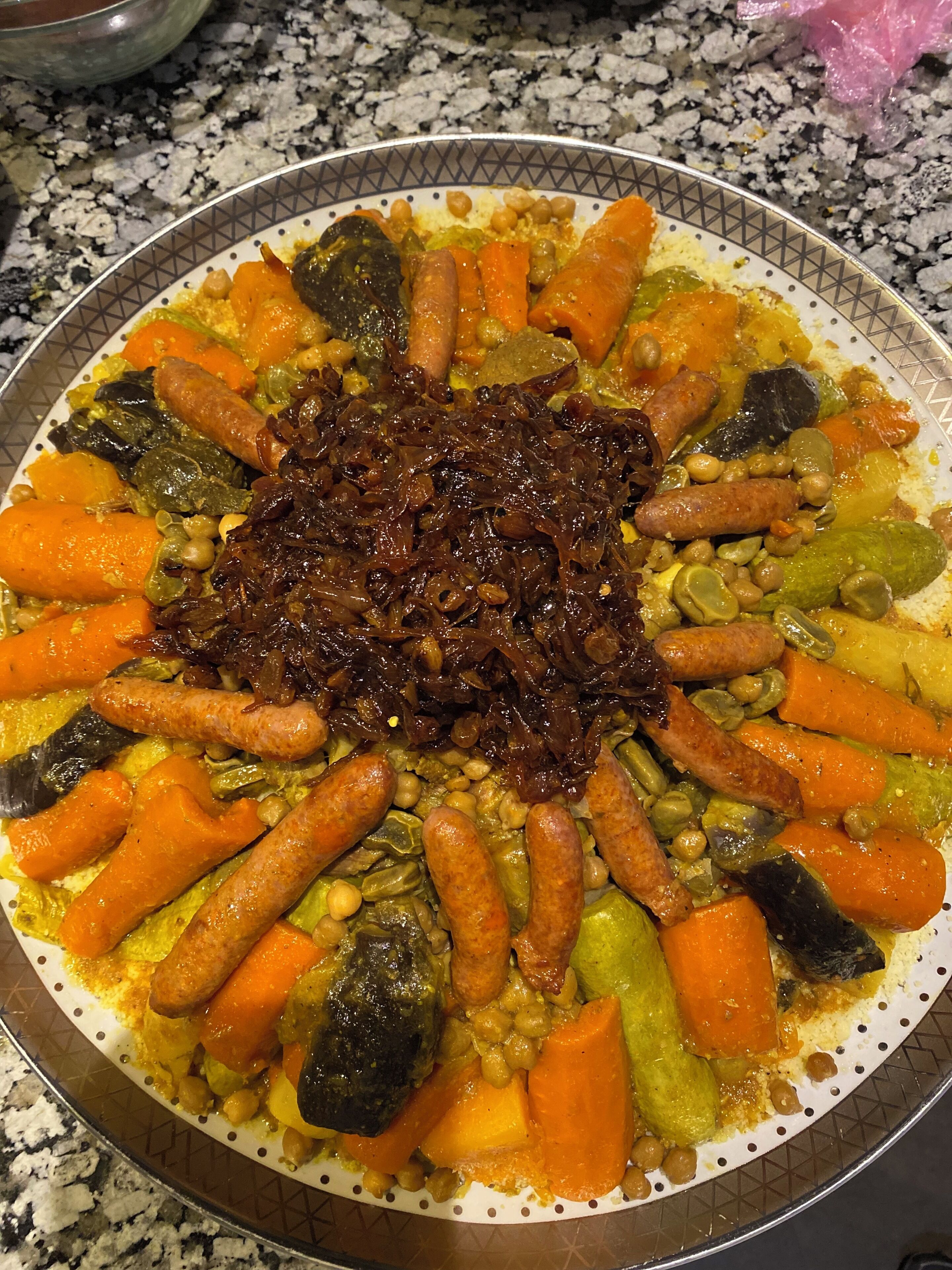 A large platter of assorted vegetables and sausages on a patterned plate.