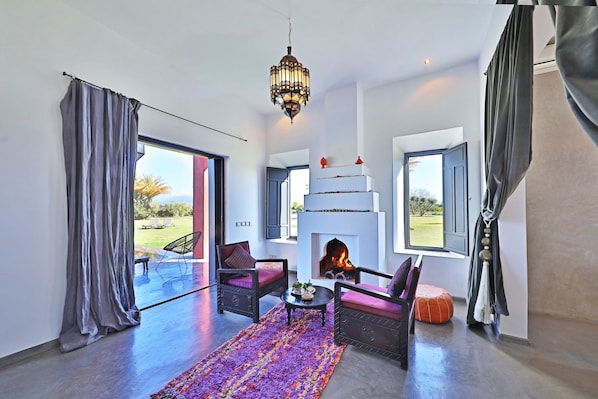 A spacious living room with a fireplace, comfortable seating, and large windows. - Dar Noujoum (Ghmate)