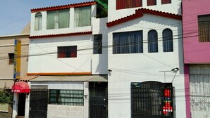 Un edificio de dos pisos con fachada blanca, detalles en rojo y varias ventanas.