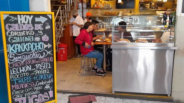 Un menú en una pizarra colgada frente a un restaurante, con diversos alimentos enumerados.