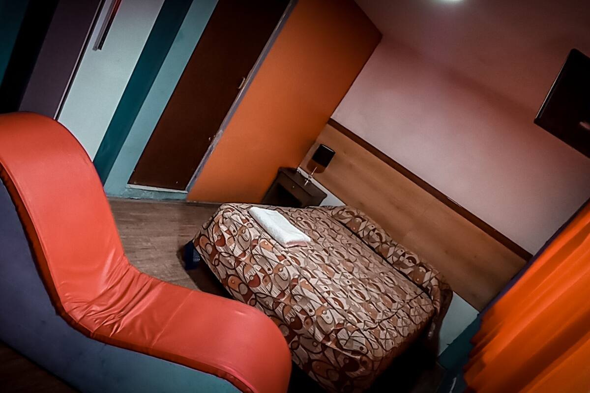 Hotellihuoneessa on sänky, tuoli, pieni pöytä ja seinälle asennettu televisio.