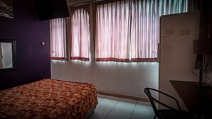 Un dormitorio con cama, escritorio, silla y ventana con cortinas.