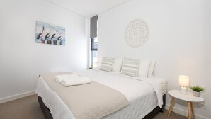 Ein schlicht eingerichtetes Schlafzimmer mit einem großen Bett, einem Vogelgemälde, einer Wanddekoration und einem Nachttisch mit Lampe und Pflanze.