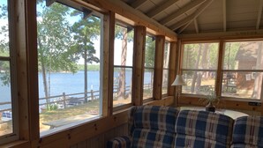 A cabin with a plaid sofa facing a large window overlooking a lake and dock. - Charming Cedar Lakeside Cottage at Elbert's Resort (Saint Germain)