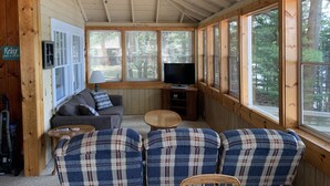 A cozy cabin interior with a ceiling fan, a television, a sofa, and plaid chairs. - Charming Cedar Lakeside Cottage at Elbert's Resort (Saint Germain)