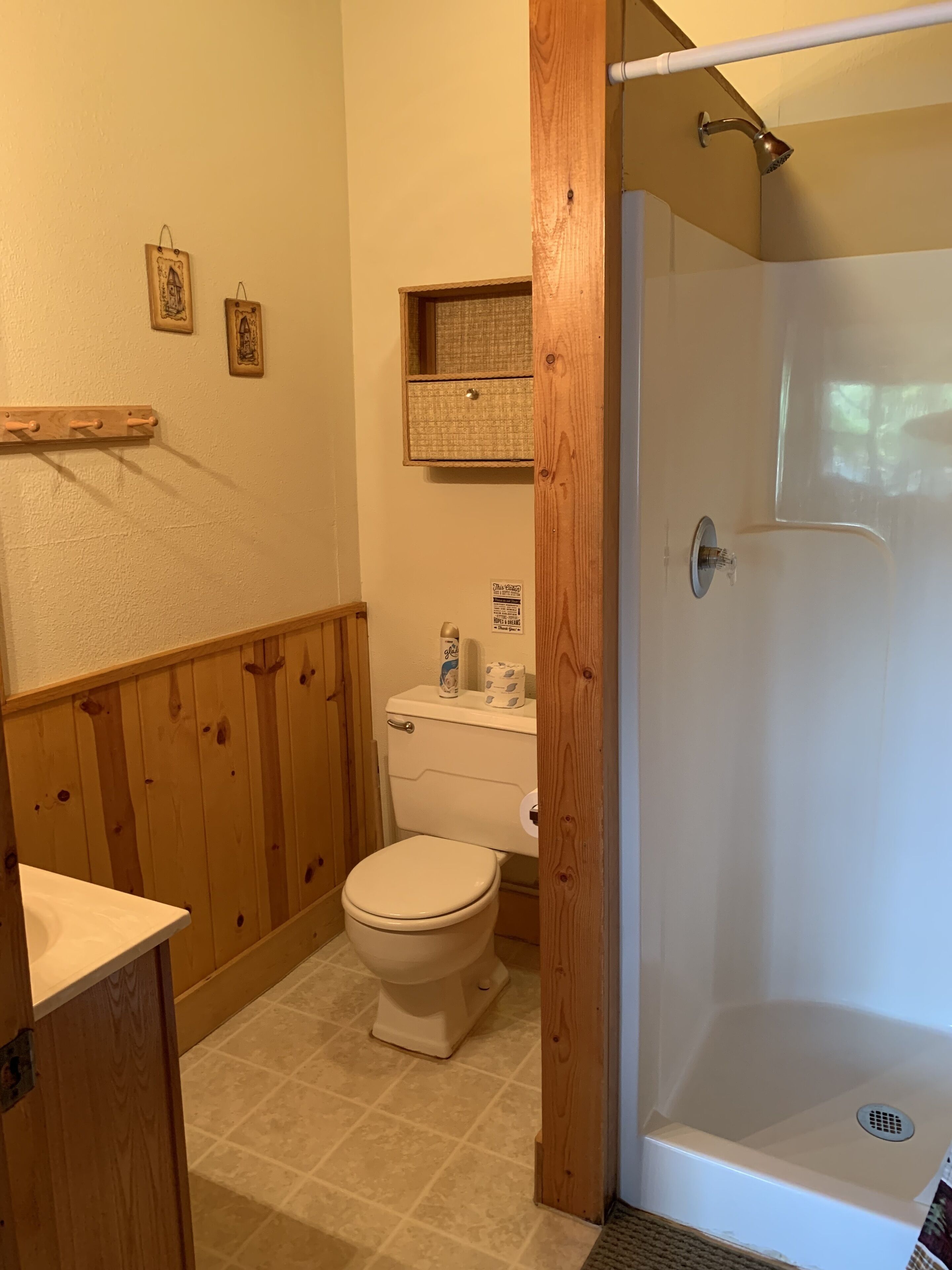 Une salle de bain avec des toilettes, une douche, un lambris en bois et une étagère avec des serviettes.