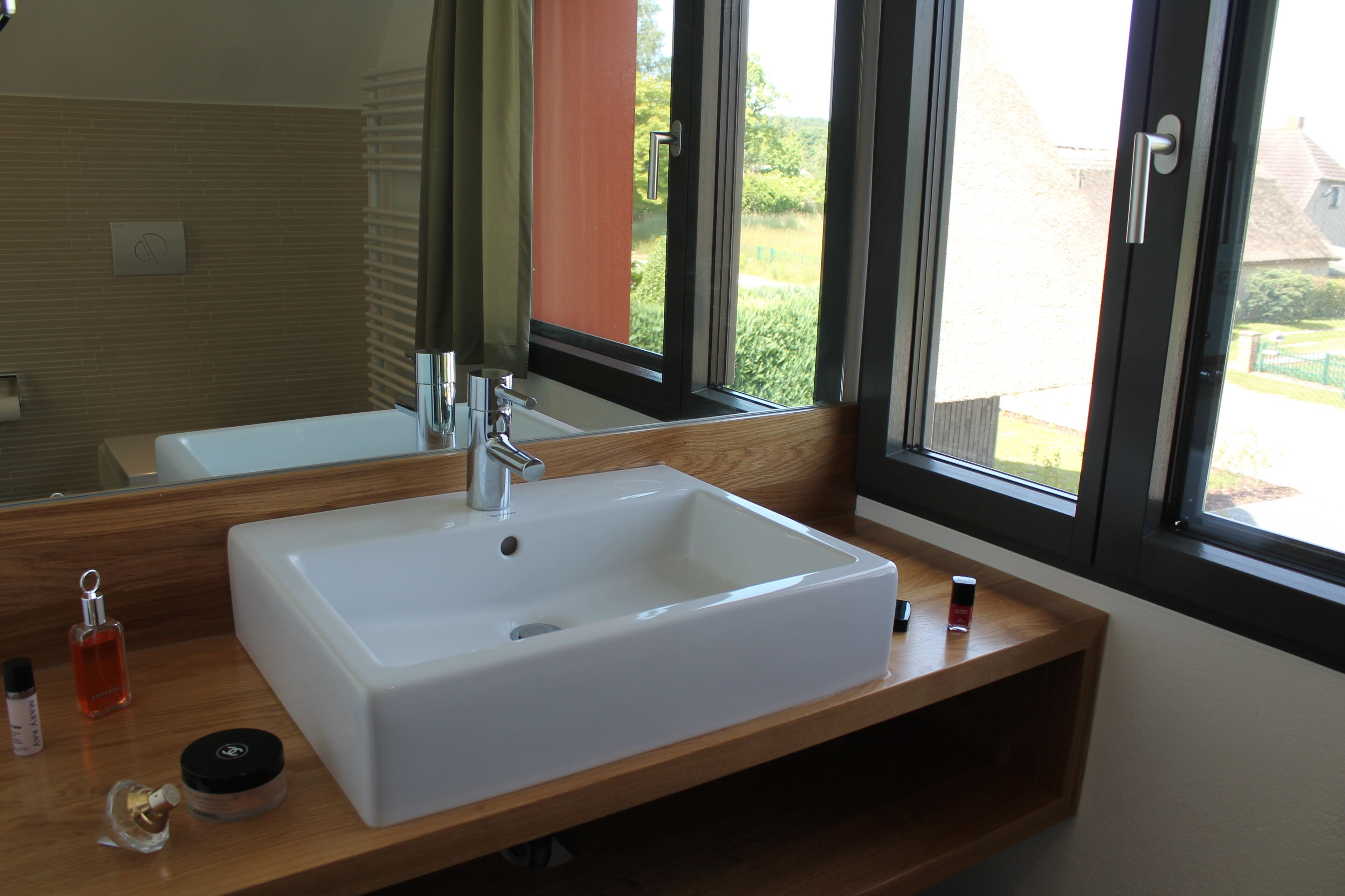 A modern bathroom with a large white sink, a mirror, and a window with a view of greenery outside.