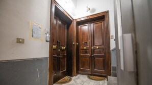 A hallway with wooden double doors, a marble floor, and a light switch on the wall. - Nidomare (Salerno)