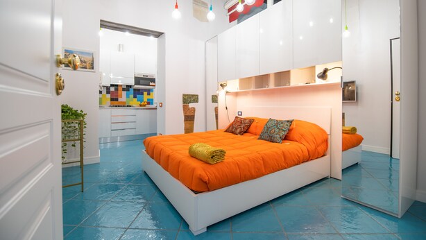 A modern bedroom with a large bed, a mirror, and a view into the kitchen. - Nidomare (Salerno)