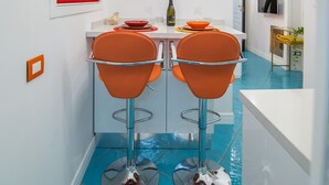 A narrow hallway with a dining area featuring two orange chairs and a white table. - Nidomare (Salerno)