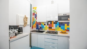 A compact kitchen with white cabinets, a colorful tile backsplash, a microwave, and a gas stove. - Nidomare (Salerno)