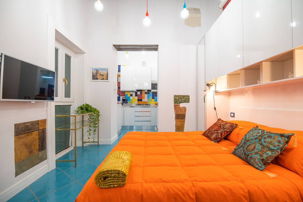 Une chambre d’hôtel compacte comprenant un grand lit, une télévision, un petit coin cuisine et un balcon agrémenté d’une plante.