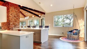 A spacious kitchen with a stone accent wall, a large island, and a hanging chair.