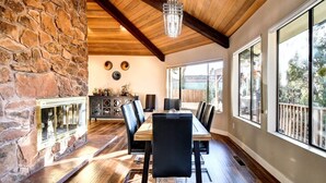 A dining area with a stone wall, wooden ceiling beams, a chandelier, and large windows.
