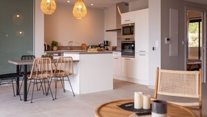 Een moderne keuken met witte kastjes, een centraal eiland en een eethoek met rieten stoelen.