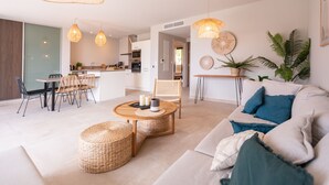 Een moderne woonkamer met een bank, salontafel en stoelen. Achtergrond toont een keuken met een eethoek.