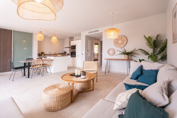 A modern living room with a sofa, coffee table, and chairs. There is a kitchen in the background with a dining area.