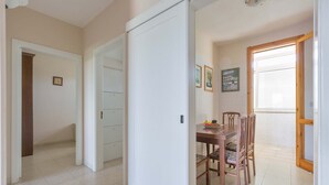 A hallway leading to a dining area with a table and chairs, a white door, and a window with a view. - 3010 Appartamento Kalos by Barbarhouse (Melendugno)