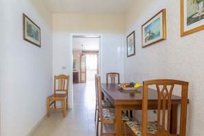 Uma área de refeições com uma mesa e cadeiras de madeira, uma tigela de frutas e quadros nas paredes.