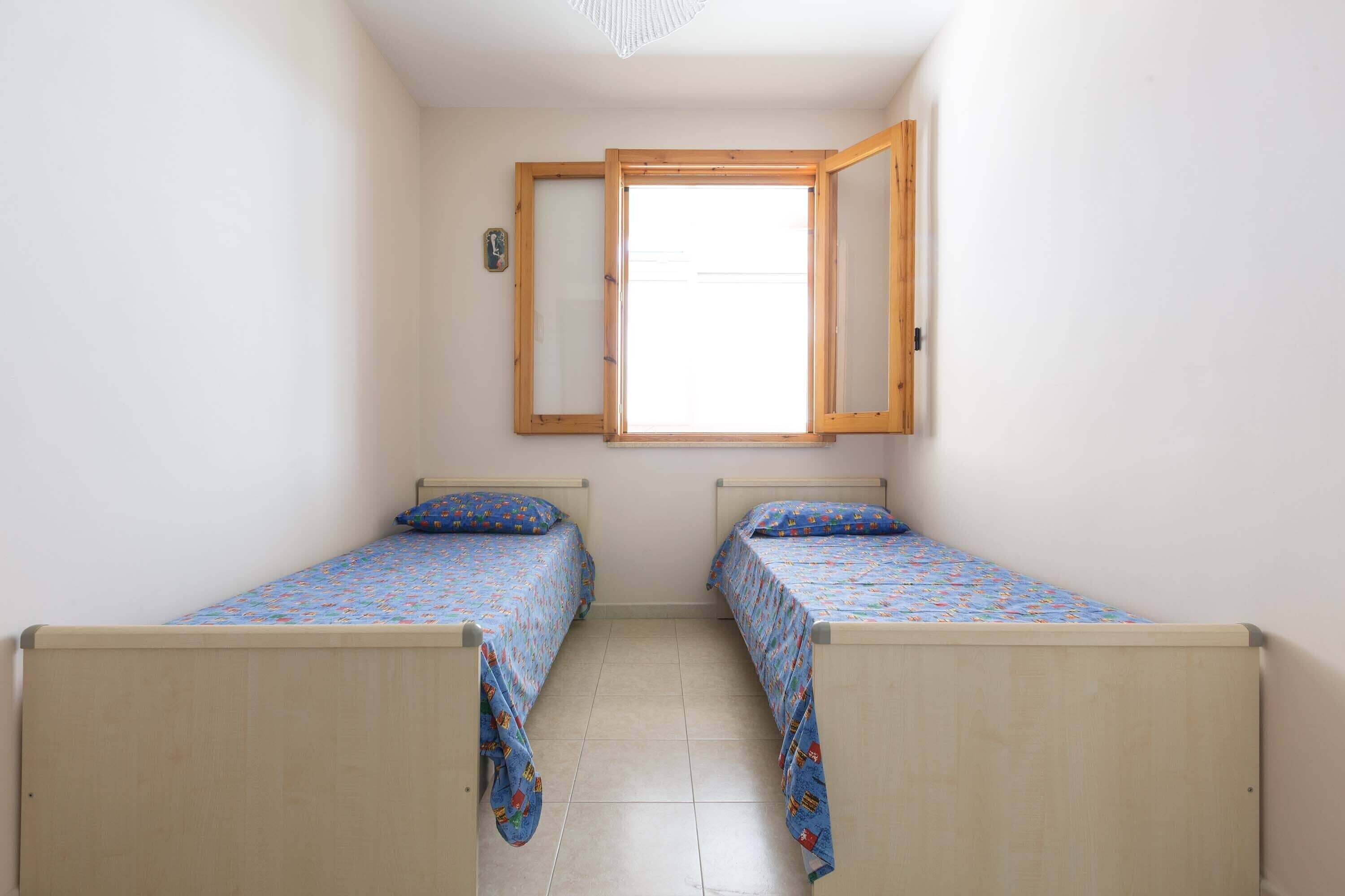 Een kleine kamer met twee houten bedden, een raam met houten kader, en een spiegel aan de muur bevestigd.