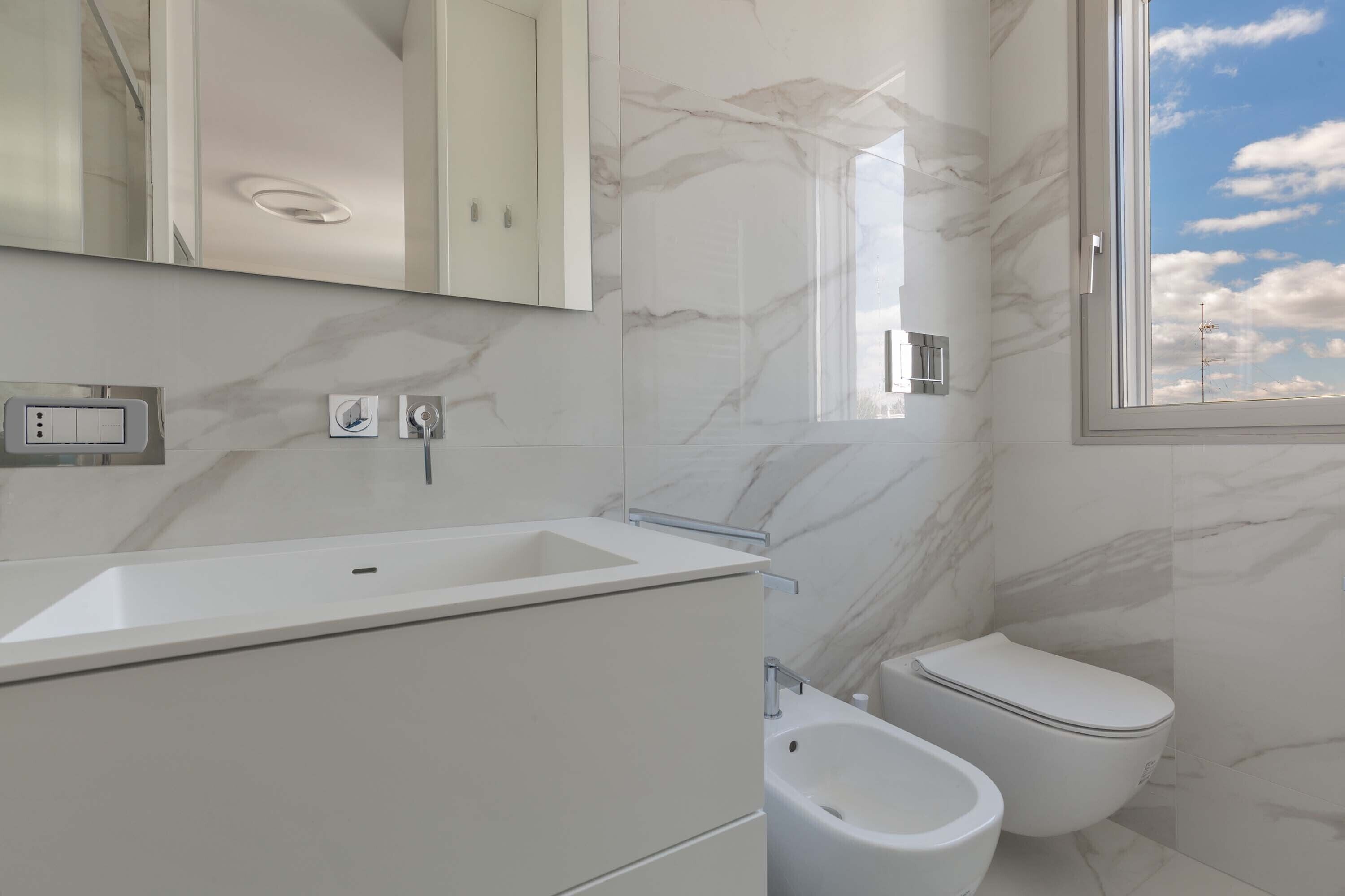 Ein modernes Badezimmer mit Marmorfliesenspiegel, einem weißen Waschbecken, einer Toilette und einem Bidet.