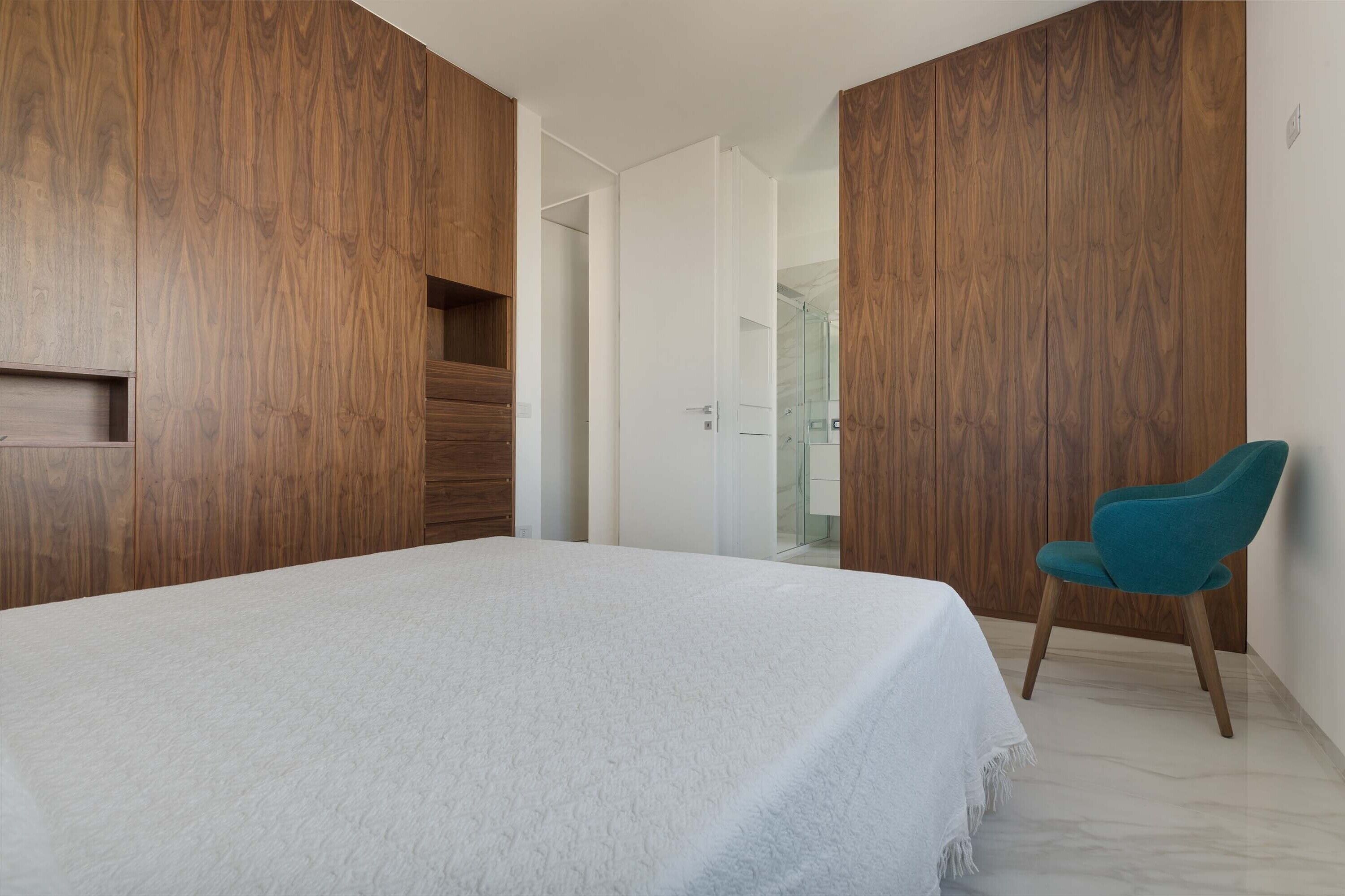 A bedroom with a bed, a chair, and wooden wardrobe units.