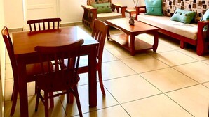 A dining area with a wooden table and chairs, a sofa with patterned cushions, and a ceiling fan.